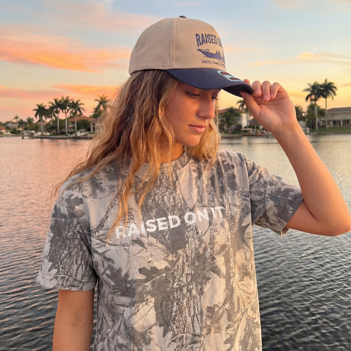 Woman wearing the Outboard Legacy Skiff hat by the water at sunset