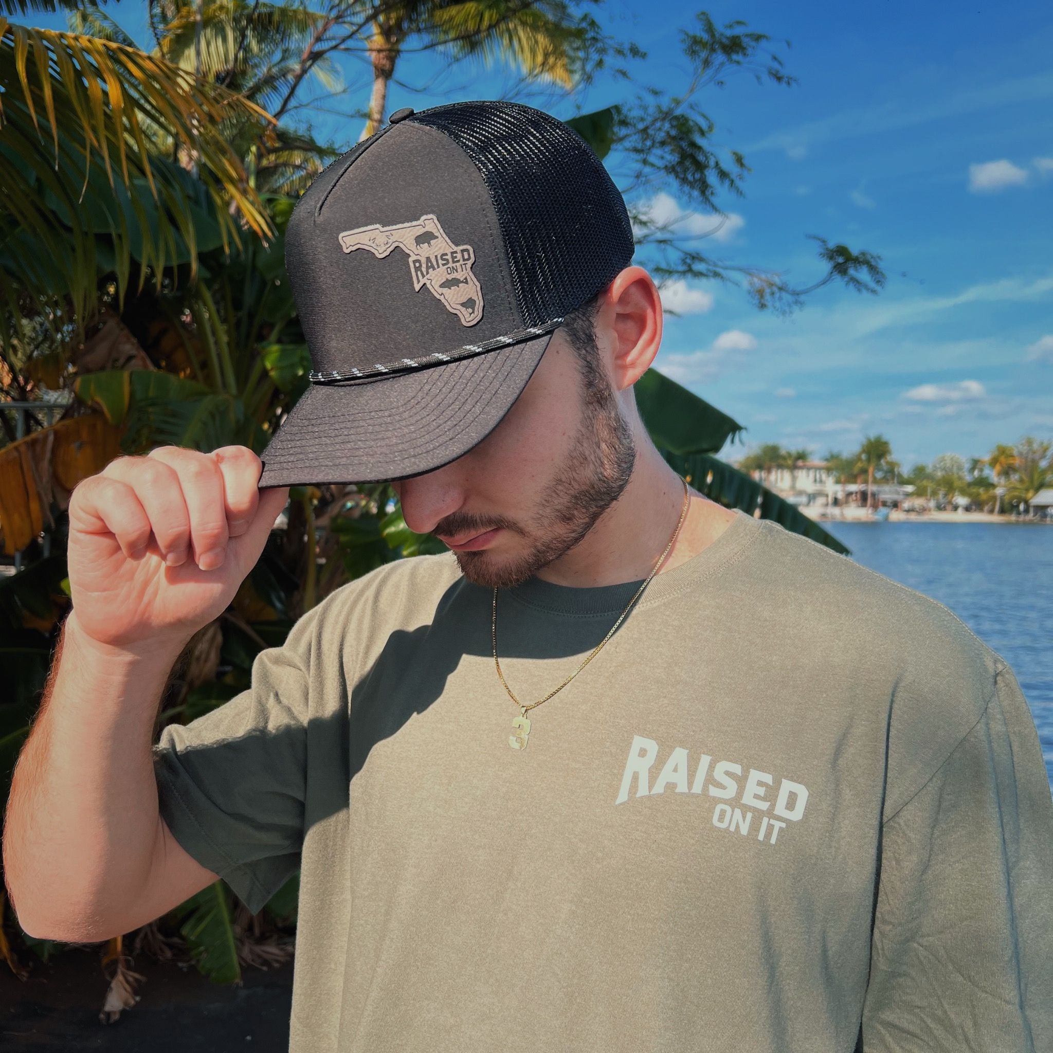 Man wearing the olive Florida Sportsman Tee, front view with Raised On It left-chest logo and trucker hat