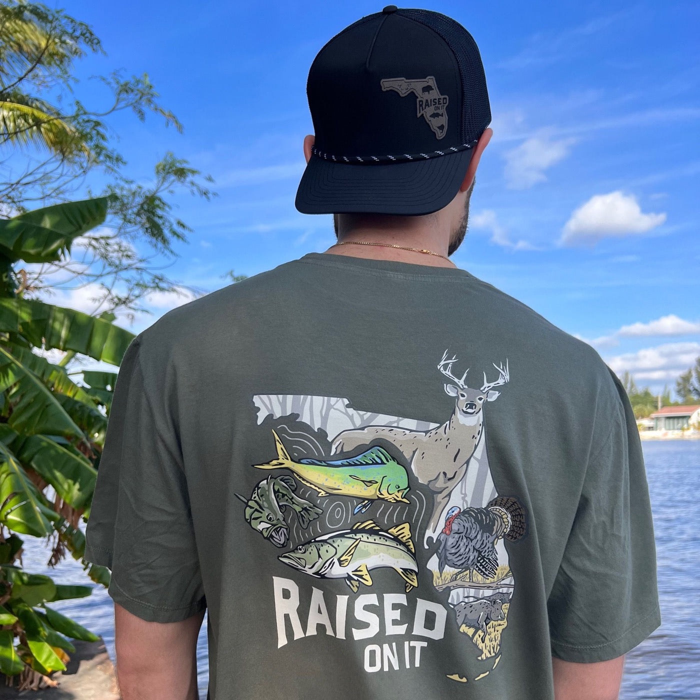 Man at the lake wearing the olive Florida Sportsman tee and a Raised On It rope hat